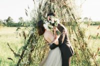 19 a creative teepee wedding altar made of branches covered with greenery and some dried grasses for a fall boho wedding