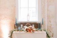 20 a colorful sweetheart table with greenery, blooms, blue candles and an arrangement of copper candle lanterns in front of the table