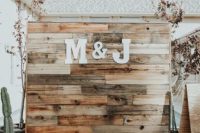 23 a simple rustic wedding backdrop of stained reclaimed wood, with monograms, a boho rug and a cactus next to it