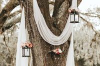 26 white airy fabric on a living tree, with candle lanterns decorated with bright blooms and a hoop