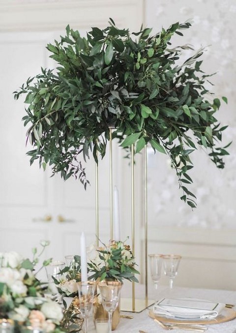 a tall centerpiece on a gold stand with lush greenery is an elegant modern idea