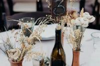 a beautiful rustic wedding centerpiece of rust-colored vases, dried blooms, bunny tails, berries, a candle and olive branches is amazing