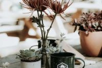 a bold eclectic wedding centerpiece of potted succulents, some blooms in a bottle and a tin mug is awesome