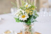 a casual backyard wedding centerpiece of a wood slice, a jar with wildflowers and greenery and a wooden heart tag