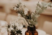 a casual backyard wedding centerpiece of apothecary bottles, thistles, willow, white blooms and a gilded pear