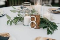 a casual backyard wedding centerpiece of greenery, pillar candles and a wooden table number is chic and stylish