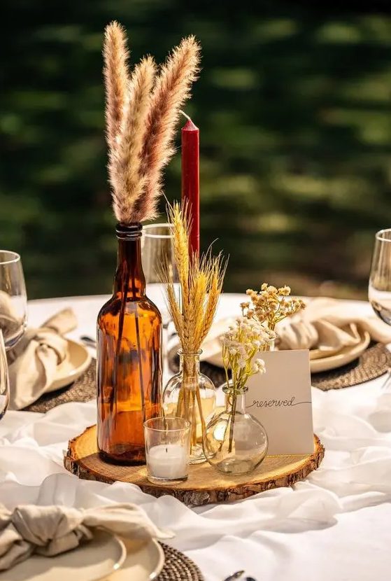 a cluster rustic fall wedding centerpiece of dried grasses and blooms and some candles is an easy to realize idea
