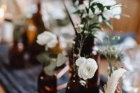a cluster wedding centerpiece of apothecary bottles, white blooms, freenery and feathers is a lovely idea for a boho wedding