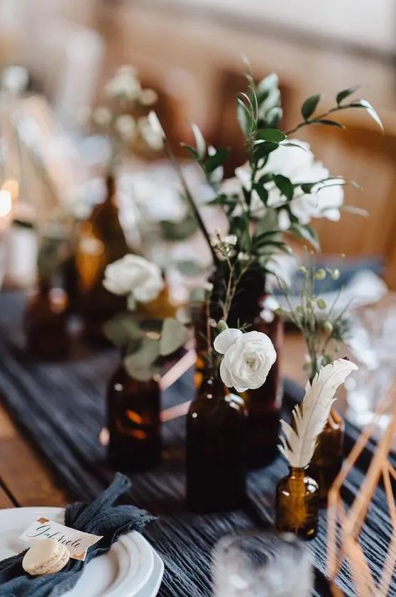 a cluster wedding centerpiece of apothecary bottles, white blooms, freenery and feathers is a lovely idea for a boho wedding
