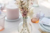 a delicate dried flower centerpiece of a bottle with dried pink blooms and some grass is a chic solution for a spring wedding