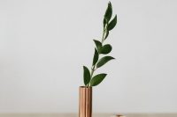 a minimalist wedding centerpiece of a copper vase and a single greenery branch plus candles all around