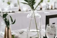 a modern clsuter wedding centerpiece of a clear and copper vase with greenery and a black and white table number for a modern wedding