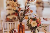 a pretty and bright fall boho wedding centerpiece of white, pink, red, rust dried blooms, greenery, a wood slice and candleholders