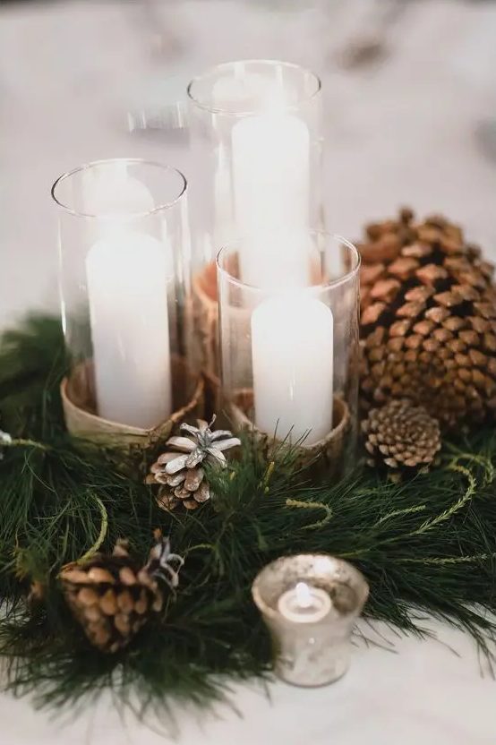 a pretty and cozy winter wedding centerpiece of evergreens, pinecones, candles in birch bark and some more lights around is amazing for a woodland or rustic celebration