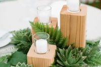 a pretty rustic wedding centerpiece of fern, leaves, succulents, wooden slabs holding candles is a lovely idea