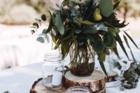 a rustic backyard wedding centerpiece of wood slices, candles, a greenery and lavender arrangement on top