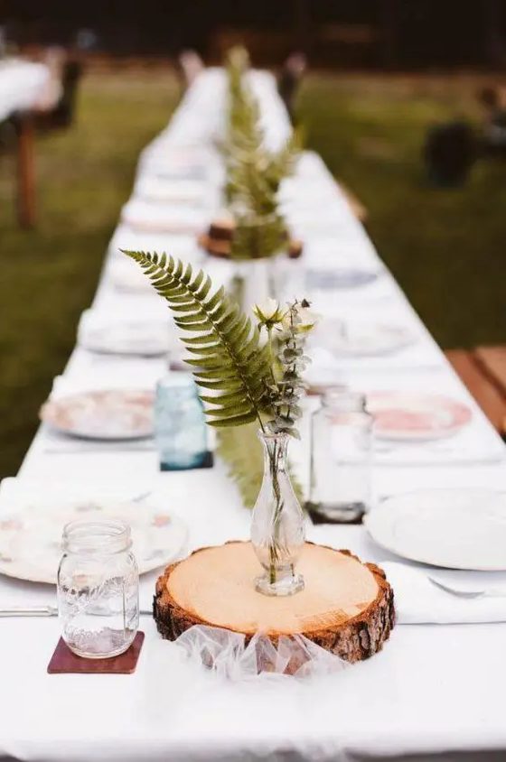a rustic wedding centerpiece of a tree slice, a vase with white blooms and fern is a lovely idea for a rustic or relaxed wedding