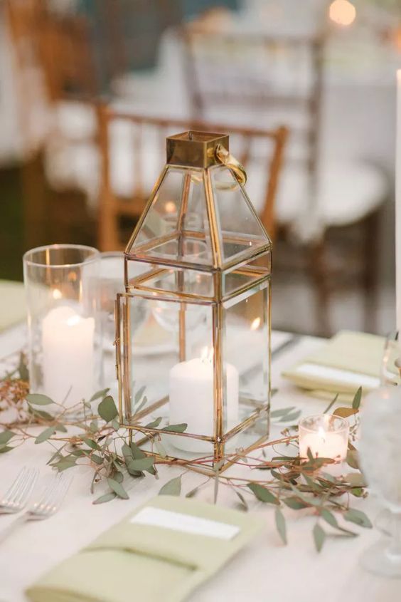 a simple and elegant backyard wedding centerpiece of candles, a copper lantern and some greenery is cool