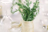 a simple backyard wedding centerpiece of a gold glitter jar and some greenery in it plus a jar with a floating candle