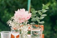 a simple rustic wedding centerpiece of a wood slice, a candleholder in lace, jars and bottles with greenery, a peony and baby’s breath