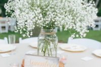 a simple wedding centerpiece of a wood slice, a jar with baby’s breath, a table number and candles
