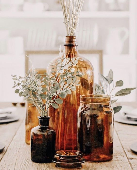 amber and brown glass bottles and jars with greenery and dried grasses is a cool and lovely wedding centerpiece