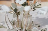 an elegant backyard wedding centerpiece of several bottles with greenery and white blooms, candles and antlers
