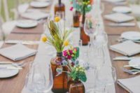 apothecary bottles and jars with colorful flowers and greenery and candles for decorating a backyard wedding table