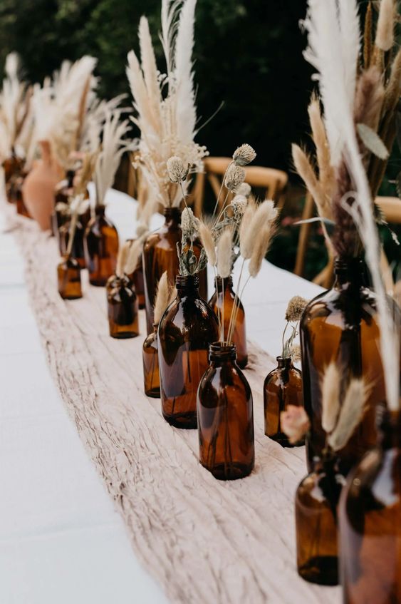 cool and very easy boho wedding centerpieces of dark bottles and dried grasses plus a fabric table runner