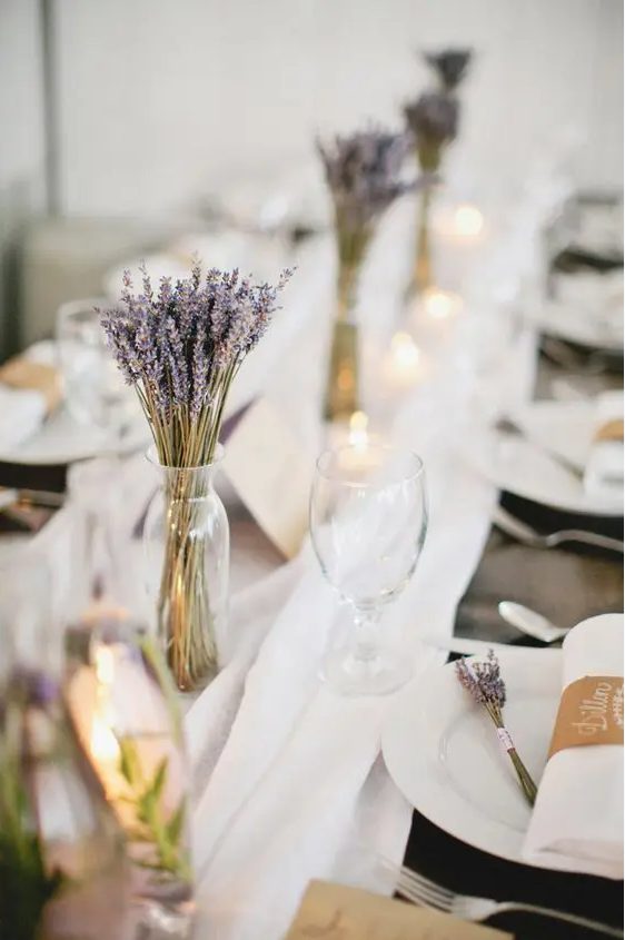 lovely lavender wedding centerpieces in sheer vases paired with candles and a white fabric runner look cute and lovely