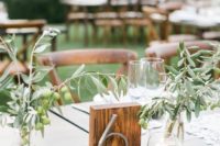 sheer bottles with olive branches and wooden table number will make up a cool table decor combo for a backyard wedding