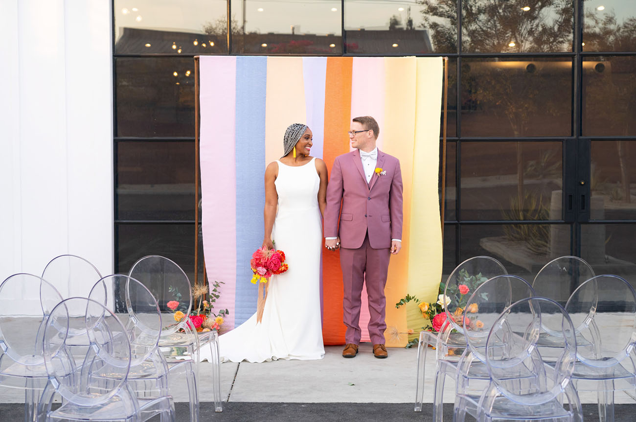 The wedding ceremony space was done with a bright striped backdrop, bright florals and sheer chairs