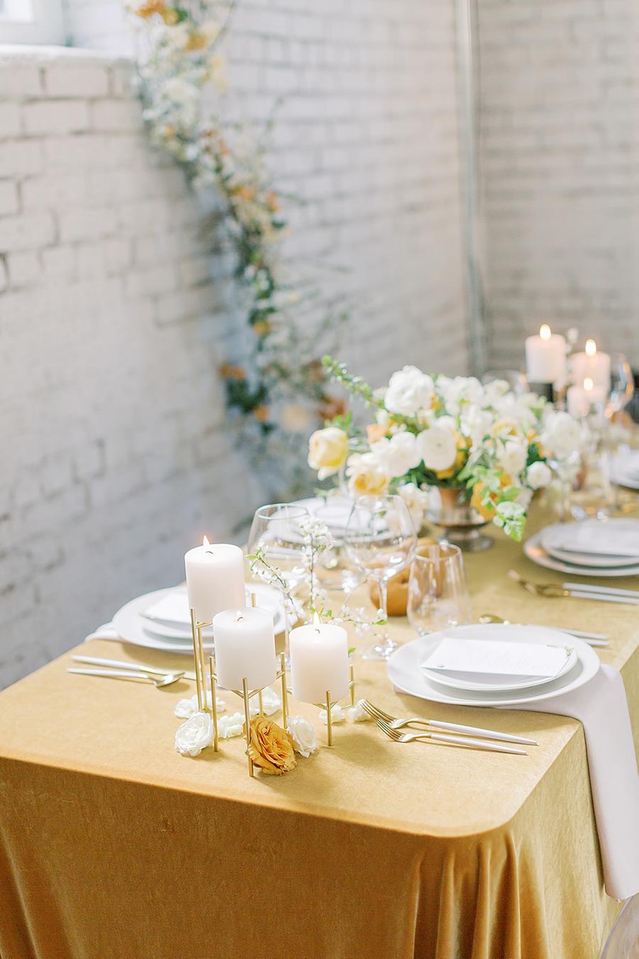 The wedding table setting was done with mustard linens, neutral and mustard blooms and pillar candles