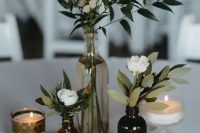 a beautiful cluster wedding centerpiece of a cleat bottle and apothecary ones, candles, greenery and white blooms is a cool solution for a boho wedding