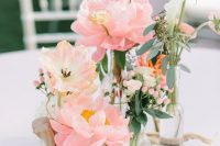 a beautiful cluster wedding centerpiece of clear bottles, blush peonies, white callas, greenery and twigs is a chic idea for spring or summer