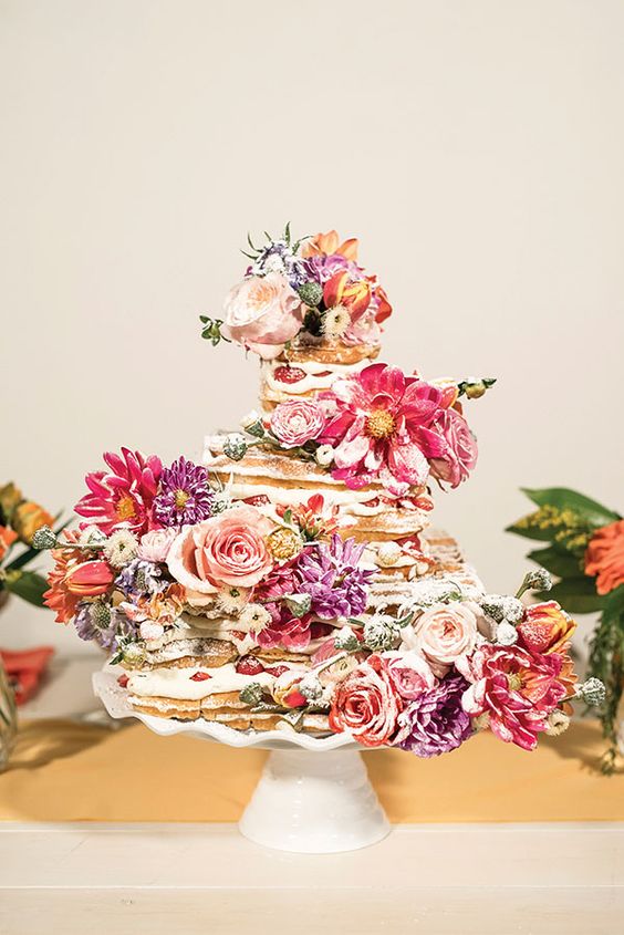 a beautiful waffle wedding cake with strawberries, pink and purple blooms and sugar powder