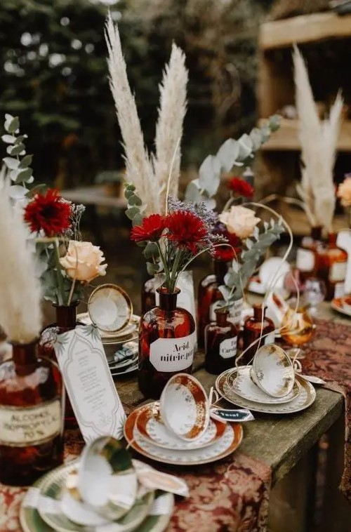 a boho cluster wedding centerpiece of apothecary bottles with neutral and burgundy blooms, eucalyptus and pampas grass is amazing
