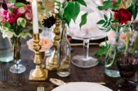 a bright and catchy cluster wedding centerpiece of bottles, glasses and blooms in various shades of pink and burgundy