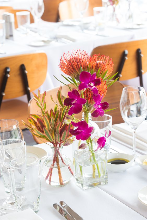 a bright tropical cluster wedding centerpiece with sheer bottles and vases and bright and bold tropical blooms