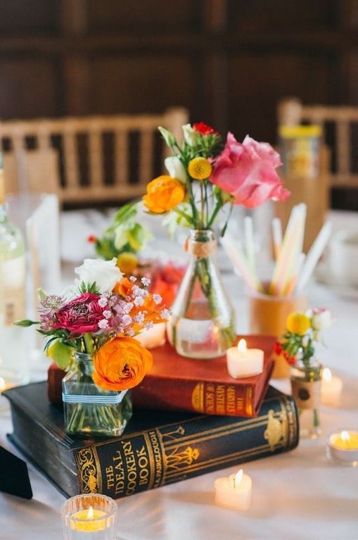 a bright wedding centerpiece of stacked books and candles, bright blooms and billy balls for a colorful summer wedding