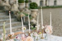 a chic cluster wedding centerpiece of sheer glass vases and bottles, with pastel blooms and tall thin candles