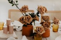 a chic cluster wedding centerpiece of terracotta vases with rust-colored roses and pink candles is great for a 70s wedding