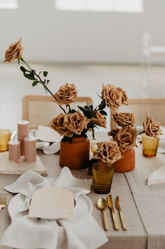a chic cluster wedding centerpiece of terracotta vases with rust-colored roses and pink candles is great for a 70s wedding