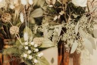 a cluster wedding centerpiece of apothecary bottles with greenery, grasses and white blooms is a lovely idea for a boho wedding