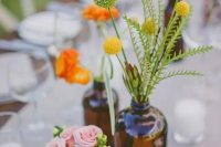 a cluster wedding centerpiece of apothecary bottles with pastel and bright blooms and greenery is a lovely idea for spring or summer