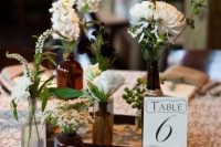 a cluster wedding centerpiece of apothecary bottles with white blooms and greenery and a table number is a nice solution for a rustic wedding