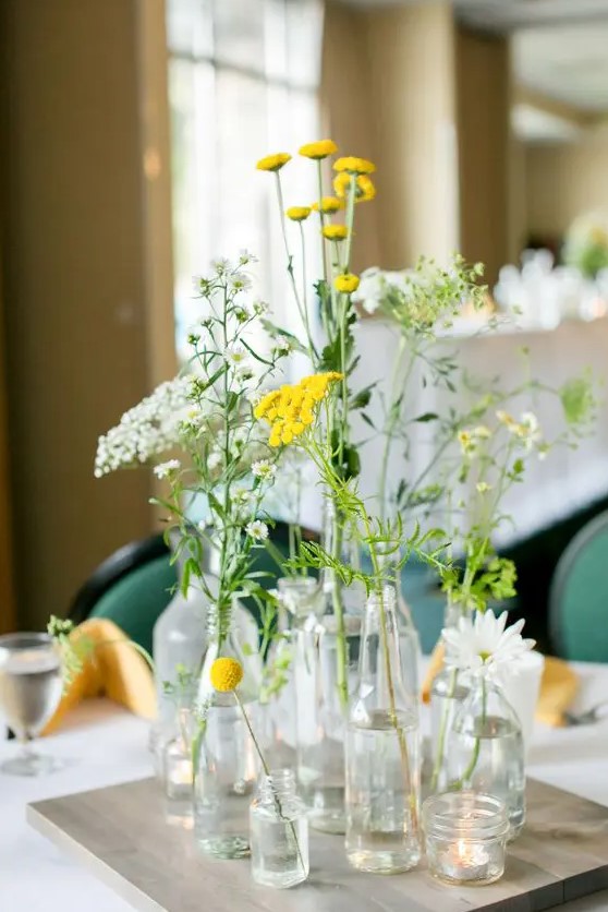 a cluster wedding centerpiece of bottles and vases, daisies and various wildflowers in white and yellow is amazing