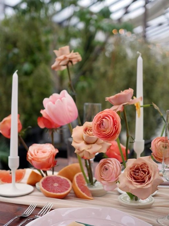 a cluster wedding centerpiece of coral, pink and peachy blooms, citrus and candles in candlesticks is lovely