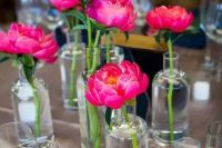 a cluster wedding centerpiece of magenta peonies and clear vases and candles is a lovely touch of color to your wedding reception