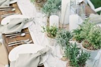 a cluster wedding centerpiece of potted greenery and succulents plus candles in large candle holders for a modern sustainable wedding